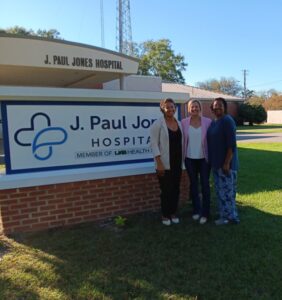three women standing in front of J. Paul Jones Hospital sign